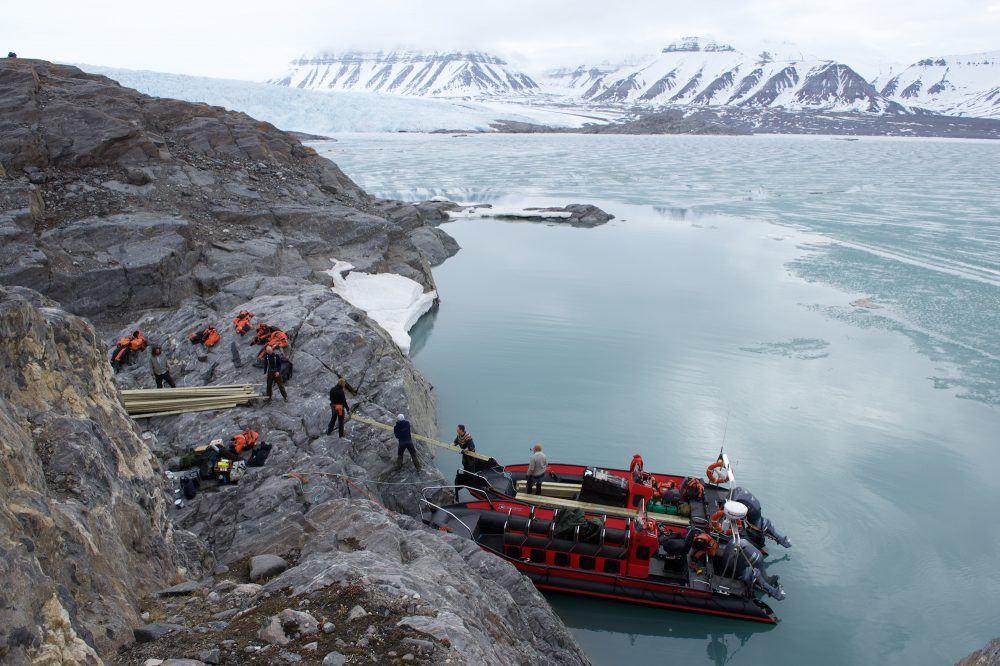 People in rib boats delivering building materials at Nordenskiöld Lodge on Svalbard.